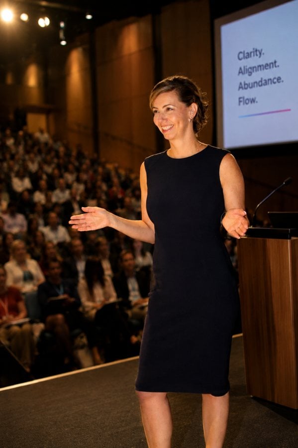 Betina speaking on stage to a large audience